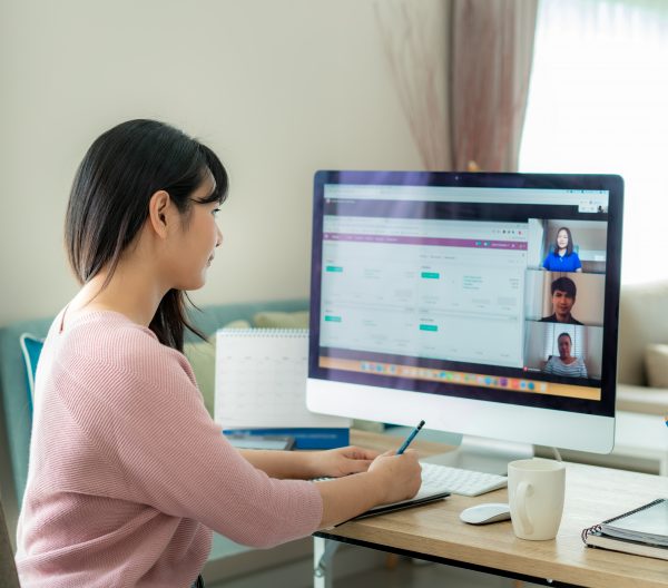 Back view of Asian business woman talking to her colleagues about plan in video conference. Multiethnic business team using computer for a online meeting in video call. Group of people smart working from home.